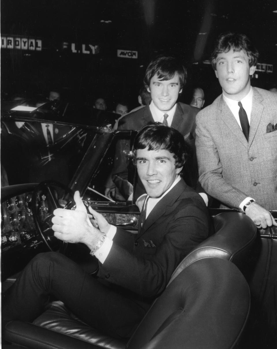 FILE--In this Oct. 19, 1965 file photo, Dave Clark, gives a thumb's up sitting in a Bentley Continental, with the other members of the band "Dave Clark Five Beat Group," Dennis Payton, left, and Mike Smith, at the International Motor Show at Earl's Court, in London. There was more to the 1960s British invasion than the Beatles, as any fan of "Catch Us If You Can" or "Because" or - get ready to shimmy - "Glad All Over." The hit tunes were among those recorded by the influential U.K. band that gets its due in "The Dave Clark Five and Beyond: Glad All Over," a PBS documentary airing Tuesday, April 8, 2014 (check local listings). (AP Photo, file)