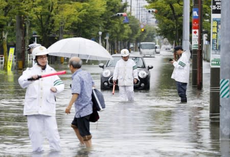 Police officers check a submerged street at a flooded area in Saga, Japan
