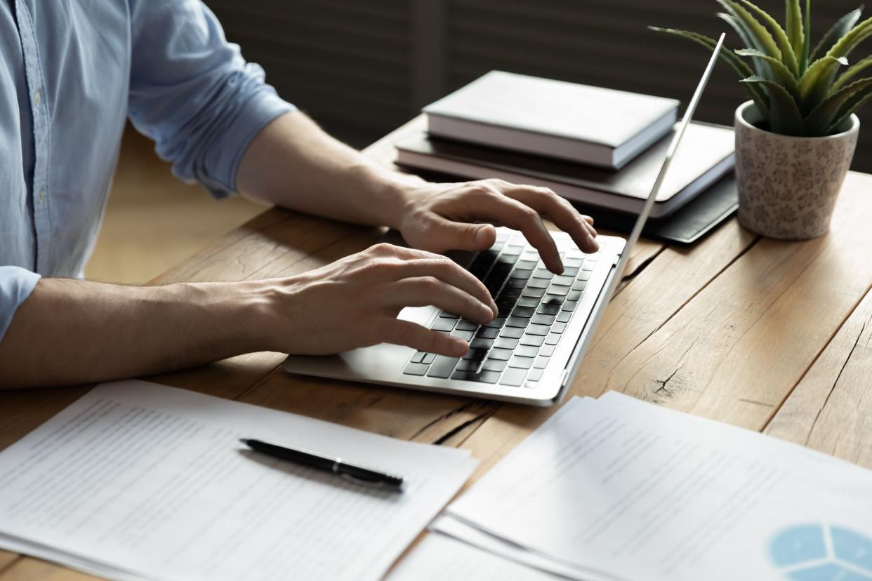 Close up businessman using laptop, typing on keyboard, sitting at wooden desk with documents, writing email, accountant writing financial report, busy student studying online, searching information