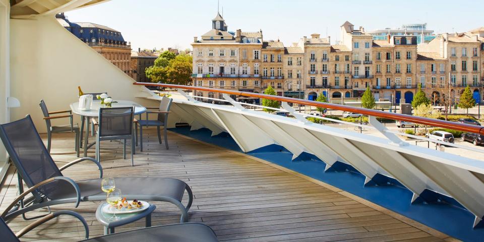 A balcony on the The World with lounge chairs and a white railing overlooking a nearby city.