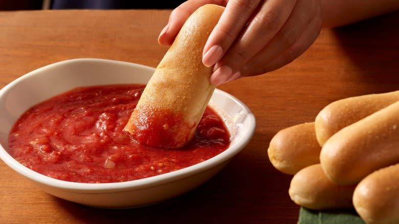 Hand dipping breadstick in marinara