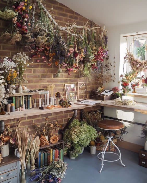 A beautiful example of cottagecore home decor, complete with ample greenery, vintage stools,, and an exposed brick wall.