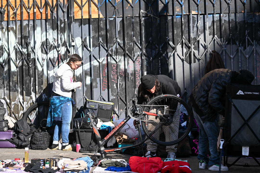 Several homeless people stand amid their possessions on a San Francisco sidewalk.