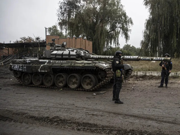 Ukrainian soldiers stand next to a damaged tank in Izyum