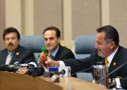 Irwindale Mayor Mark Breceda, right pulls out his personal bottle of Sriracha hot sauce to show his support to find a solution to Sriracha’s smell issue during a city council meeting in Irwindale, Calif., Wednesday, April 23, 2014. The city of Irwindale is suing the maker of Sriracha hot sauce and last week the Los Angeles suburb tentatively voted to declare the bottling plant a public nuisance. Irwindale City Attorney Fred Galante, middle, says relocating seems extreme and the city only wants to see the smell issue addressed. Manuel Garcia, Irwindale Mayor Pro Tem is at left. (AP Photo/Damian Dovarganes)