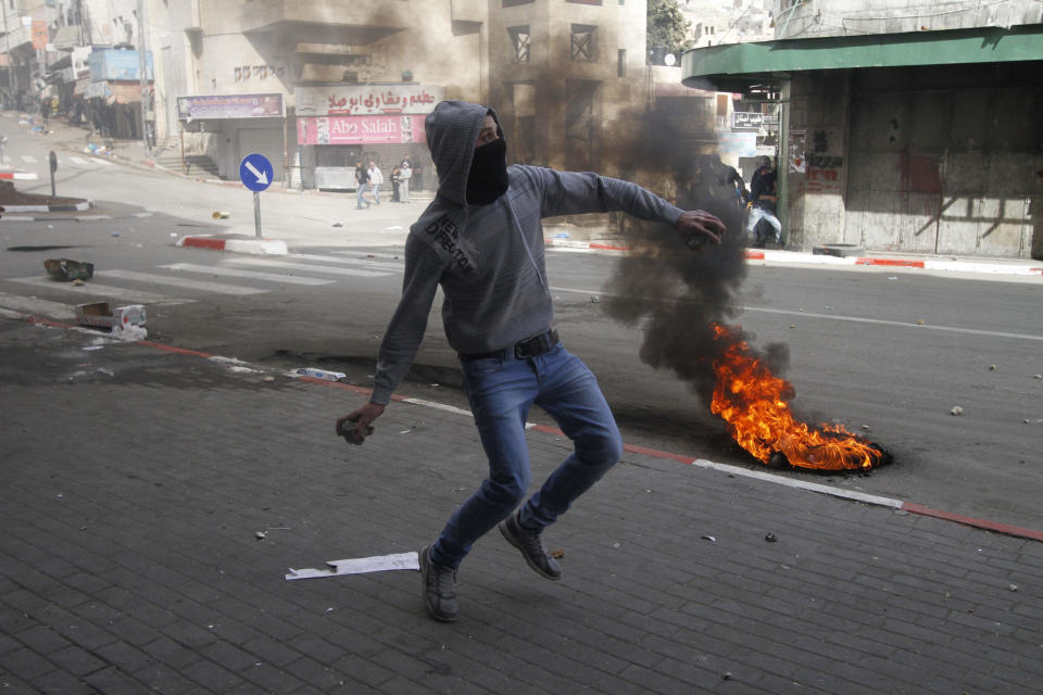 A Palestinian throws a stone towards Israeli soldiers in the center of the West Bank city of Hebron, Friday, Feb. 21, 2014, during a demonstration against the closure of the main downtown street. Shuhada street was shut after a 1994 mosque massacre when a settler shot and killed 29 Muslim worshippers. The military closed it citing security reasons. (AP Photo/Nasser Shiyoukhi)