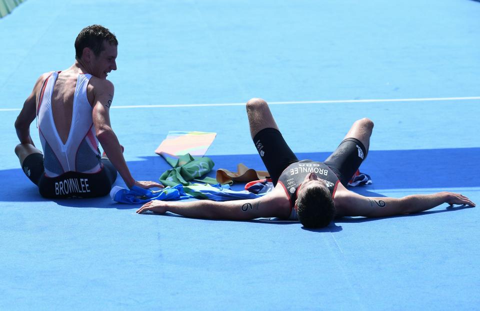 Britain's Alistair Brownlee (L) and his brother Britain's Jonathan Brownlee rest on the floor past the finish line after winning the men's triathlon at Fort Copacabana during the Rio 2016 Olympic Games in Rio de Janeiro on August 18, 2016. Alistair Brownlee won the gold medal while his brother Jonathan won silver. / AFP / Yasuyoshi Chiba        (Photo credit should read YASUYOSHI CHIBA/AFP/Getty Images)