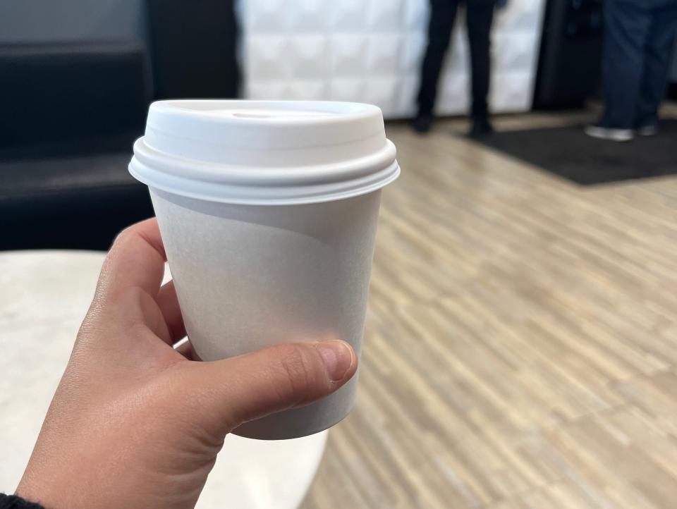 The author holding up a white coffee cup as other passengers enter the indoor lounge.