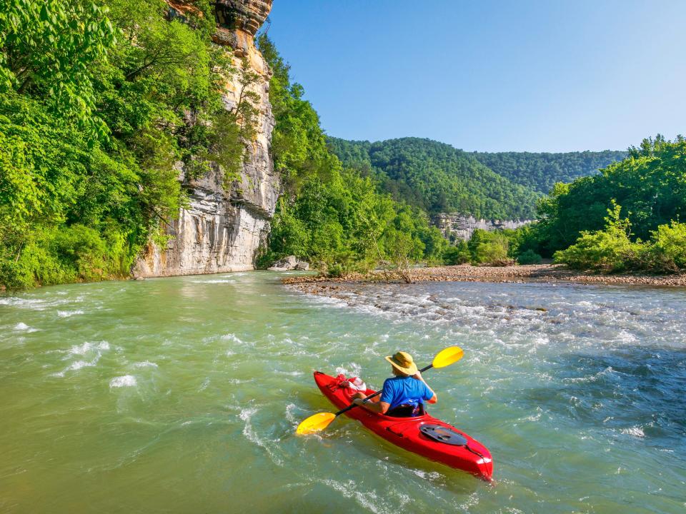 A kayaker on a river next to mountains and trees.