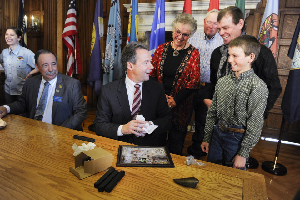 FILE - In this April 16, 2019, file photo, Luke Phipps, 12, presents Montana Gov. Steve Bullock with a fossilized rib and tail vertebrae from a triceratops at the state Capitol in Helena, Mont., after the governor signed a bill to clarify that fossils are part of a property's surface rights, not its mineral rights, unless a contract separating the ownership says otherwise. The Montana Supreme Court heard arguments Thursday, Nov. 7, 2019, on the same issue in relation to a 2014 court case over the ownership of millions of dollars of dinosaur fossils that is not affected by the new law. (Thom Bridge/Independent Record via AP, File)