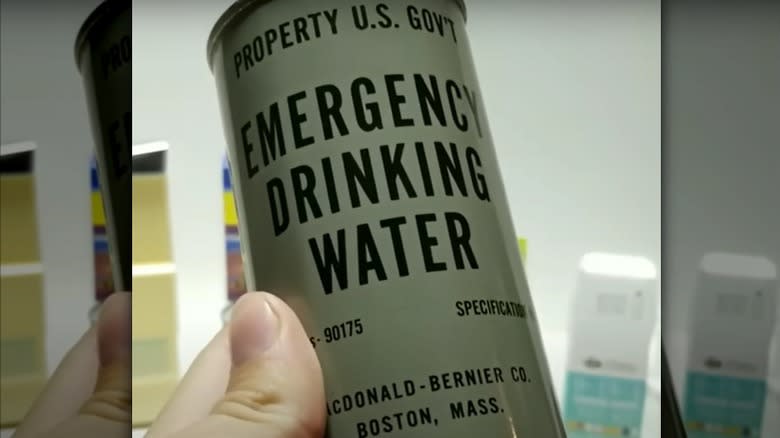 A hand holding a U.S. government-issued sealed can of water