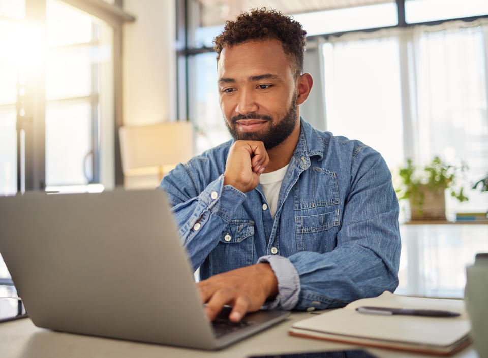 Happy businessman working on his laptop at home. Handsome businessman reading an email on his laptop at home. Freelance entrepreneur typing on his laptop at home. Virtual remote worker at home