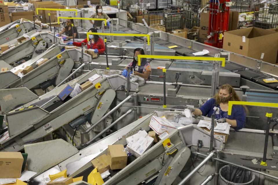 Packages move through large metal conveyor machines with a postal worker at each machine