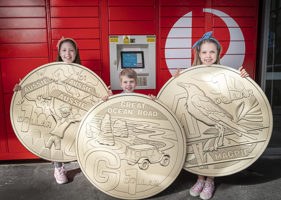 Three children, each holding a giant replica of a $1 coin