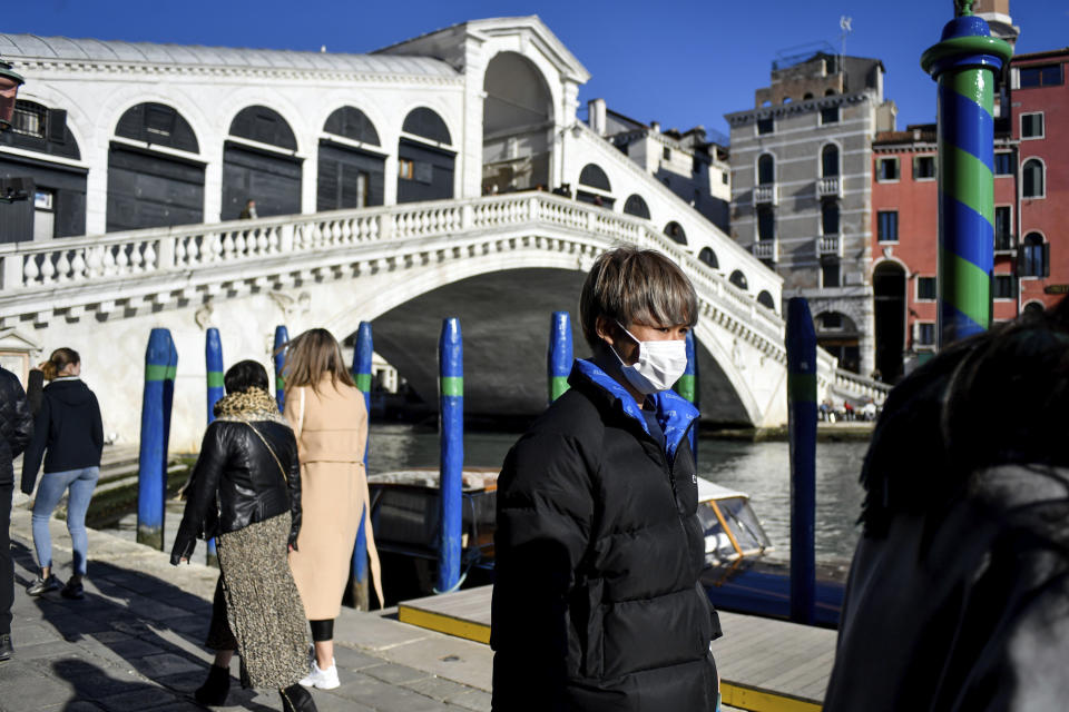 A man wearing a protective mask walks past the Ponte di Rialto (Rialto Bridge) in Venice, Italy, Friday, Feb. 28, 2020. Authorities in Italy decided to re-open schools and museums in some of the areas less hard-hit by the coronavirus outbreak in the country which has the most cases outside of Asia, as Italians on Friday yearned for a return to normal life even amid fears that the outbreak could plunge the country's economy into recession. (Claudio Furlan/Lapresse via AP)