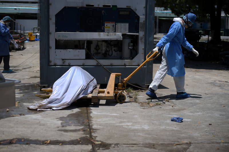 Health workers wearing protective gear bring a dead body past a refrigerated container outside of Teodoro Maldonado Carbo Hospital amid the spread of the coronavirus disease (COVID-19), in Guayaquil