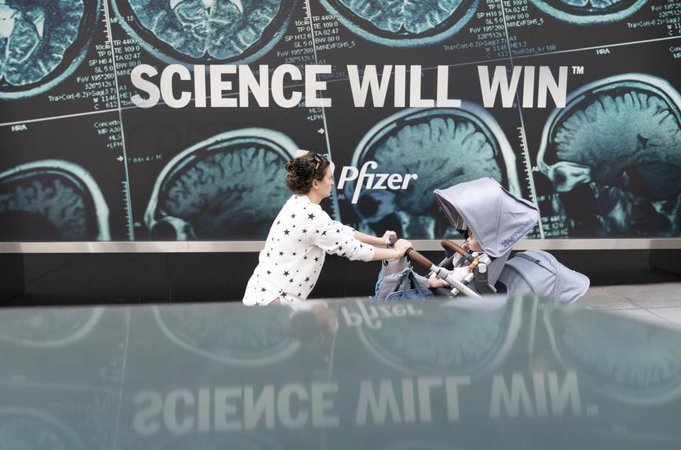 A woman pushes a baby in a stroller past a sign hanging outside Pfizer headquarters in New York, Monday, May 23