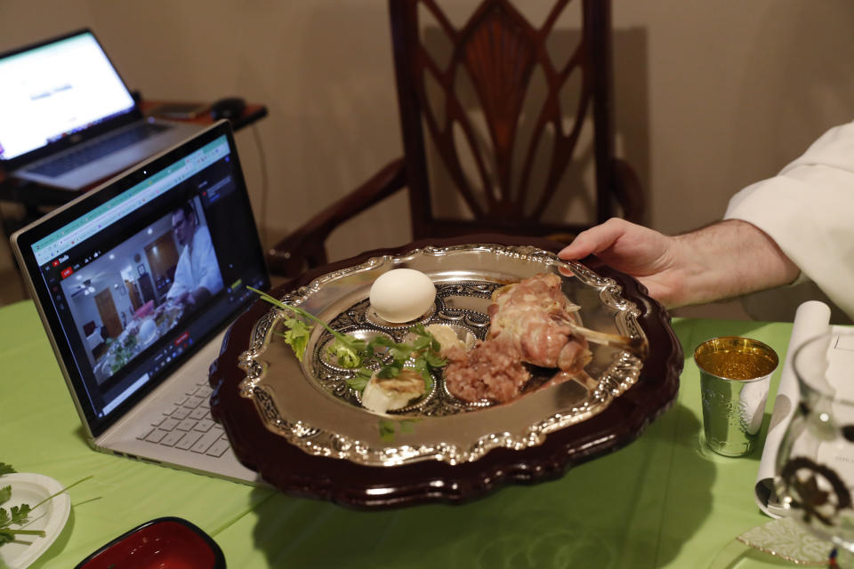 Rabbi Shlomo Segal holds a ritual seder plate in front of a computer screen while conducting a virtual Passover seder and broadcasting it on YouTube for his congregants, friends and family members in the Sheepshead Bay section of Brooklyn during the current coronavirus outbreak, Wednesday, April 8, 2020, in New York. The new coronavirus causes mild or moderate symptoms for most people, but for some, especially older adults and people with existing health problems, it can cause more severe illness or death. (AP Photo/Kathy Willens)