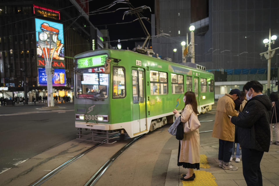 People wait for a traffic light to turn green as a tram moves through the intersecion in the Susukino district of Sapporo, northern Japan, Friday, April 14, 2023. G-7 energy and environment ministers are meeting in the city on the northern Japanese island of Hokkaido ahead of a summit next month. (AP Photo/Hiro Komae)