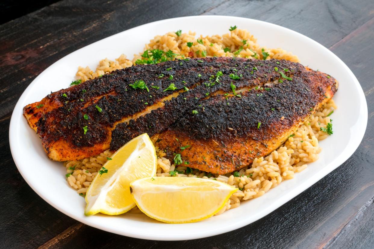 Blackened red snapper fillet served on a platter of dirty rice with lemon wedges and parsley garnish