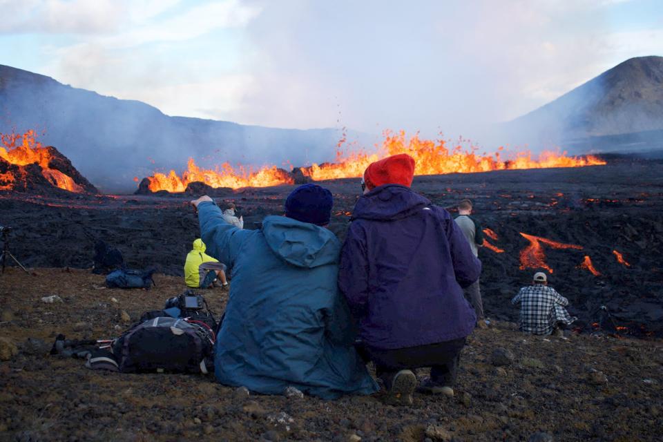 People look at the lava erupting and flowing at the scene of the newly erupted volcano at Grindavik, Iceland on August 3, 2022. - A volcano erupted on August 3, 2022 in Iceland in a fissure near Reykjavik, the Icelandic Meteorological Office (IMO) said as lava could be seen spewing out of the ground in live images on local media. The eruption was some 40 kilometres (25 miles) from Reykjavik, near the site of the Mount Fagradalsfjall volcano that erupted for six months in March-September 2021, mesmerising tourists and spectators who flocked to the scene.