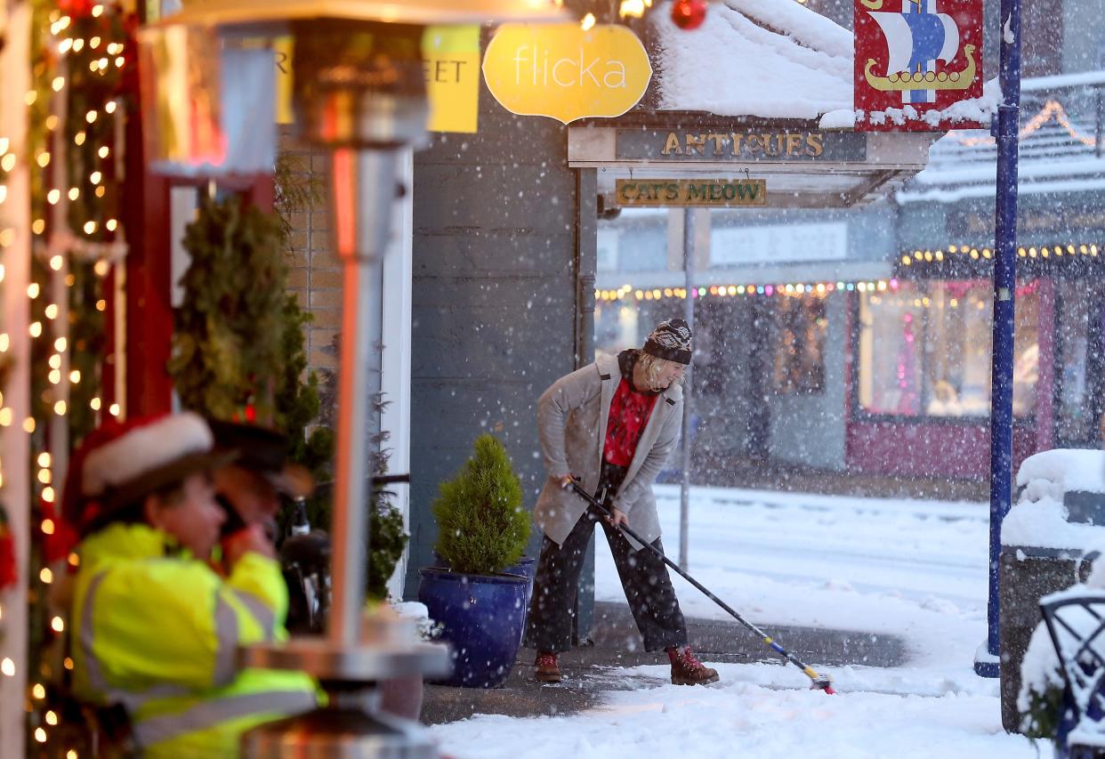 Kristin Jagodzinske uses a broom to sweep the snow off the sidewalk in front of her Flicka boutique in downtown Poulsbo on a snowy Tuesday.