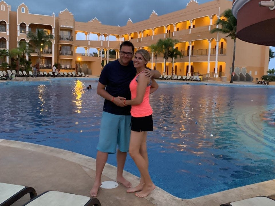 A man and woman embracing and posing in front of a hotel pool at dusk.