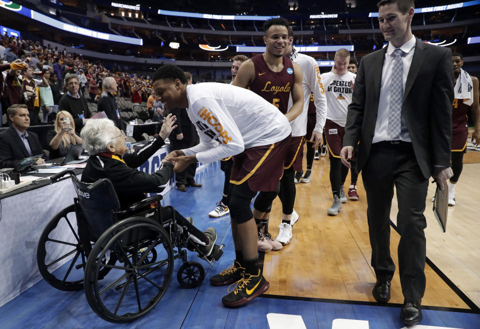 FILE - In this March 15, 2018, file photo, Sister Jean Dolores Schmidt, left, greets the Loyola Chicago basketball team as the Ramblers walk off the court after a win over Miami in a first-round game at the NCAA college basketball tournament in Dallas. Loyola Chicago is back in the tournament. And Sister Jean will be there, too. The 101-year-old team chaplain's lobbying paid off Tuesday, March 16, when the school reversed course and announced she will go. That means she gets to watch her beloved Ramblers in person for the first time this season when No. 17 Loyola meets Georgia Tech in Indianapolis on Friday. (AP Photo/Tony Gutierrez, File)