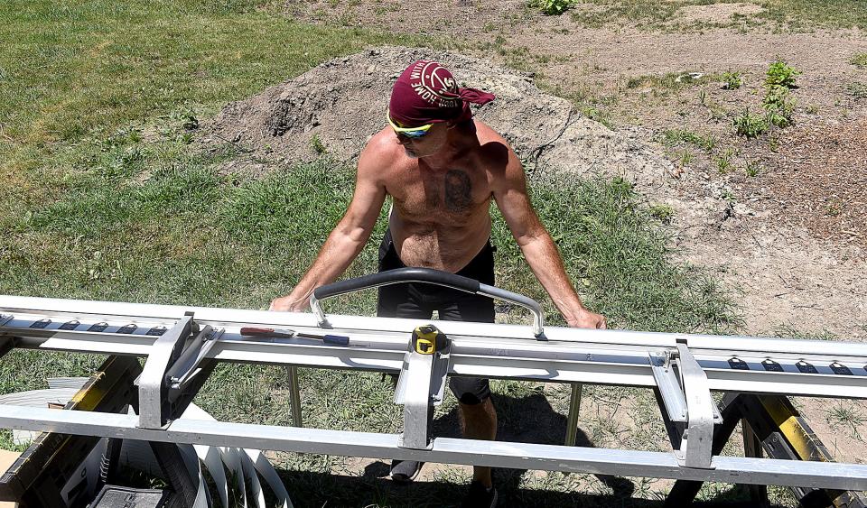 Brian Davis, owner of Imagine Property Group in Ashland, bends a piece of flashing for windows on a house at Rogers Street and College Avenue on Tuesday as the temperature rose near 100 degrees.