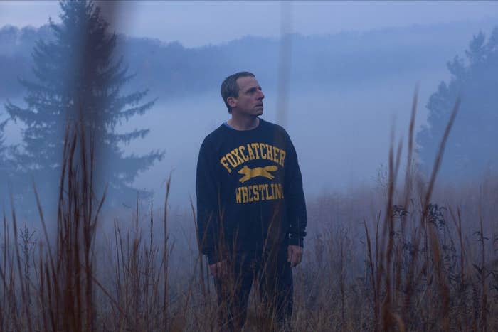 An older man in a blue wrestling sweatshirt stands in a foggy field