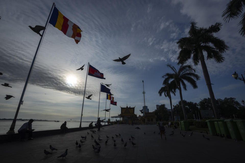 Tourists sit near a Buddhist temple with pigeons flying alongside the Tonle Sap river as flags of various countries participating in the Association of Southeast Asian Nations (ASEAN) summit fly in Phnom Penh, Cambodia, Thursday, Nov. 10, 2022. Southeast Asian leaders hold meetings with various groups ahead of the summit opening on Friday. (AP Photo/Anupam Nath)
