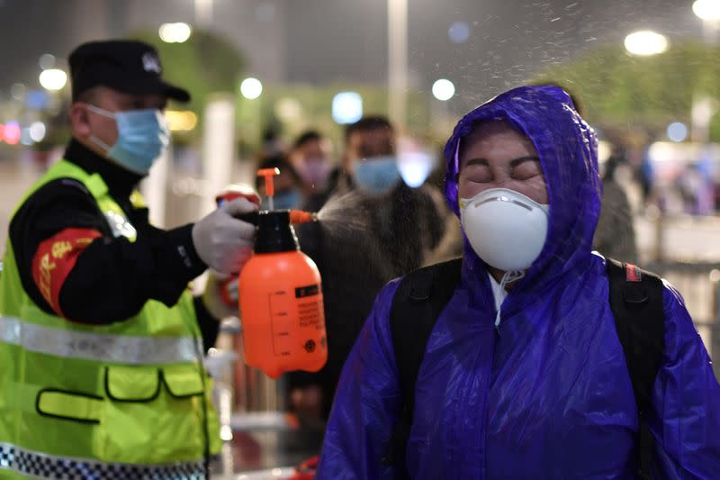 Police officer sprays disinfectant on a traveller outside Hankou Railway Station in Wuhan