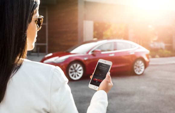 A woman unlocks her Model 3 with a Tesla app on her smartphone.