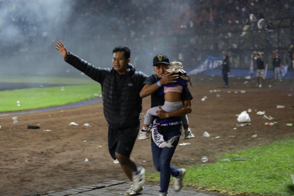 Football fans evacuate a girl during a clash between fans at Kanjuruhan Stadium (EPA)