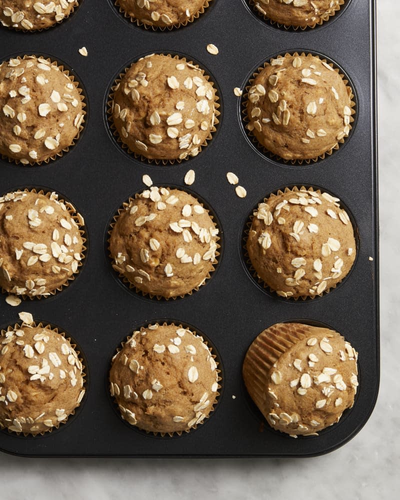 An overhead view of a muffin tin full of baked applesauce muffins with oats on top