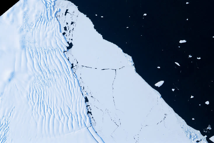 The edge of an ice shelf with fractures and rifts, sea ice and icebergs floating on the ocean