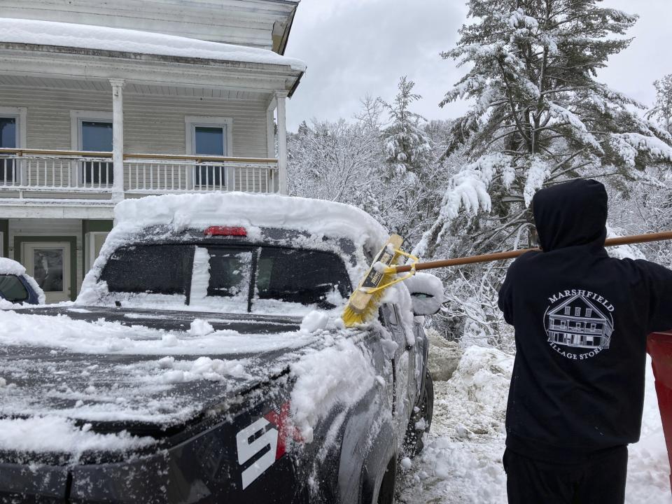 Jack Whalen brushes snow off his truck with a push broom in Marshfield, Vt., Tuesday, March 14. 2023. (AP Photo/Lisa Rathke)
