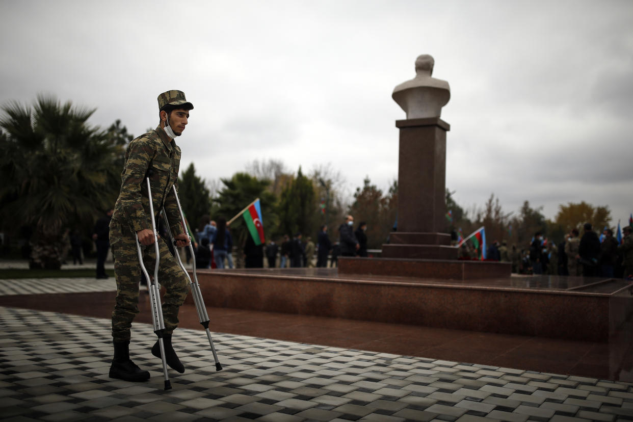 A wounded Azerbaijani soldier stand next to a bust of Azerbaijani President Ilham Aliyev's father and former Azerbaijani President Heydar Aliyev, as people celebrate the transfer of the Lachin region to Azerbaijan's control, as part of a peace deal that required Armenian forces to cede the Azerbaijani territories they held outside Nagorno-Karabakh, in Aghjabadi, Azerbaijan, Tuesday, Dec. 1, 2020. Azerbaijan has completed the return of territory ceded by Armenia under a Russia-brokered peace deal that ended six weeks of fierce fighting over Nagorno-Karabakh. Azerbaijani President Ilham Aliyev hailed the restoration of control over the Lachin region and other territories as a historic achievement. (AP Photo/Emrah Gurel)