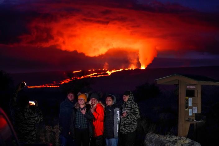 People pose for a photo in front of lava erupting from Hawaii's Mauna Loa volcano Wednesday, Nov. 30, 2022, near Hilo, Hawaii (AP)