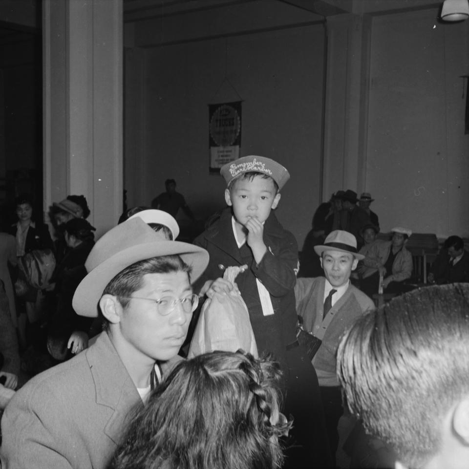 In this photo provided by the National Archives, a boy wearing a "Remember Pearl Harbor" hat and his family arrive at 2020 Van Ness Avenue in San Francisco, as part of the contingent of 664 residents of Japanese ancestry first to be relocated from the city on April 6, 1942, to an internment camp for Japanese Americans during World War II. (Dorothea Lange/War Relocation Authority/National Archives via AP)