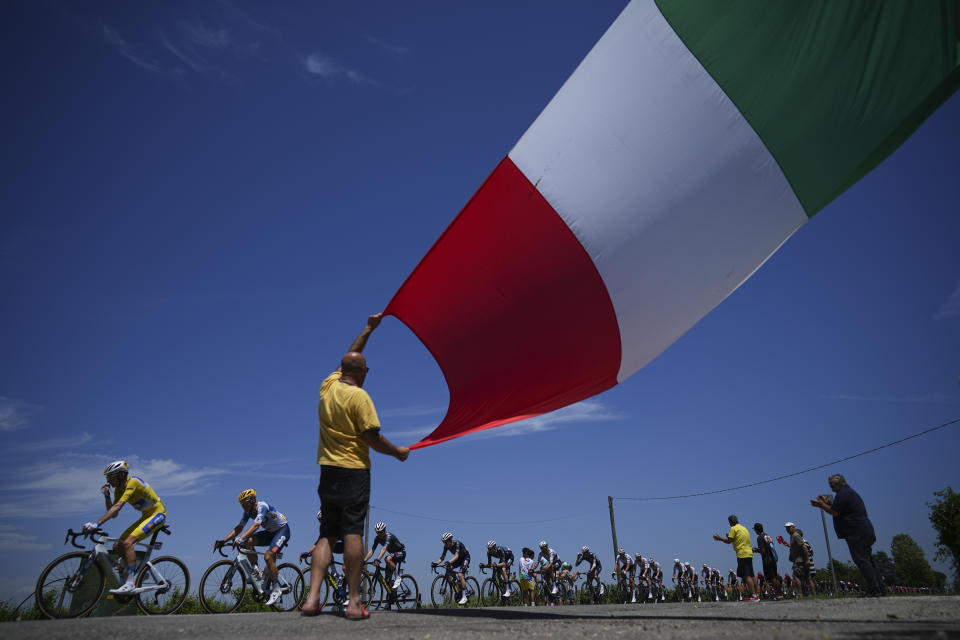 A cycling fan waves the Italian flag as the pack with France's Romain Bardet, wearing the overall leader's yellow jersey, left, passes during the second stage of the Tour de France cycling race over 199.2 kilometers (123.8 miles) with start in Cesenatico and finish in Bologna, Italy, Sunday, June 30, 2024. (AP Photo/Daniel Cole)