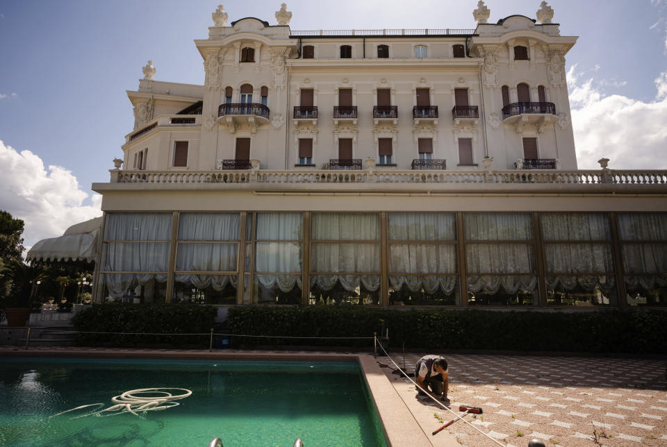 In this Monday, May 11, 2020 photo a man does maintenance work by a swimming pool of the Rimini Grand Hotel, in Rimini, Italy. The luxury Liberty-style hotel, where carnivalesque Italian director Federico Fellini used to stay, was built in 1908. Parts of the hotel were recreated in Rome's Cinecittà film studios for some of his movies including 'Amarcord' (1973). (AP Photo/Domenico Stinellis)