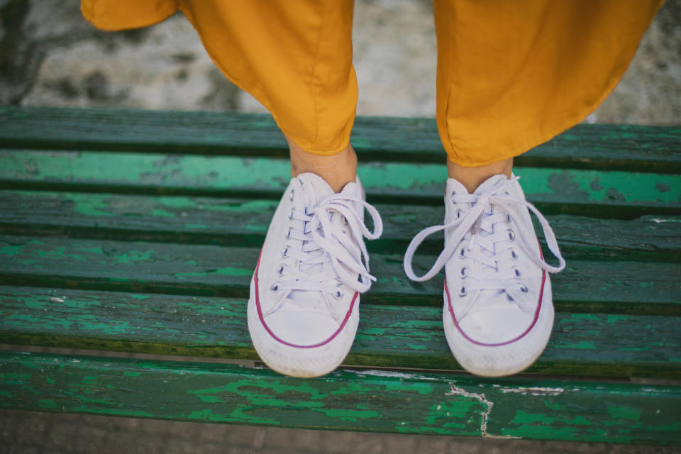 Person in yellow pants standing on a green bench, wearing white sneakers