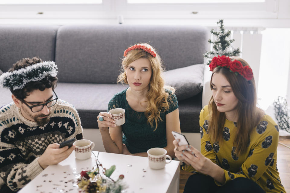 Annoyed young woman sitting between her friends looking at her smartphones