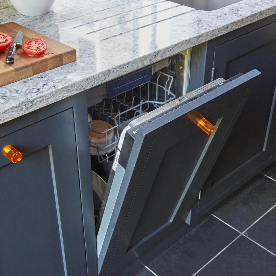 An open dishwasher in a dark blue kitchen