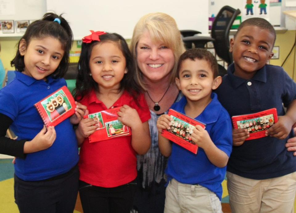 Volunteer Lisa Link poses with pre-K kids at Cambridge Early Learning Center last year. The students are holding books Link made after they performed a play at the school. Link, a freelance photographer, took pics of the performance and gave students personalized books so they could see themselves performing