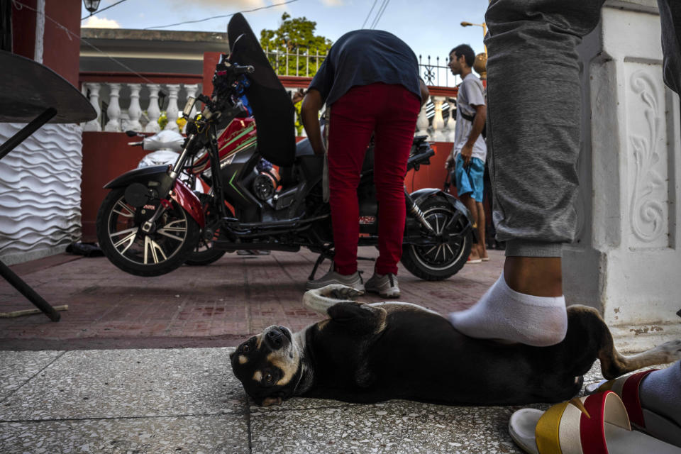 Kiera gets a foot rub at his home by his care taker as people work on their electric scooters after attending a gathering in the capital for stunts and races in Cojimar, Cuba, Friday, July 15, 2022. Cuba has been flooded in recent years with “motorinas”, as these electric scooters are called on the island, a fad for many, but also a solution to the transportation problems and fuel shortages that overwhelm the Caribbean nation. (AP Photo/Ramon Espinosa)