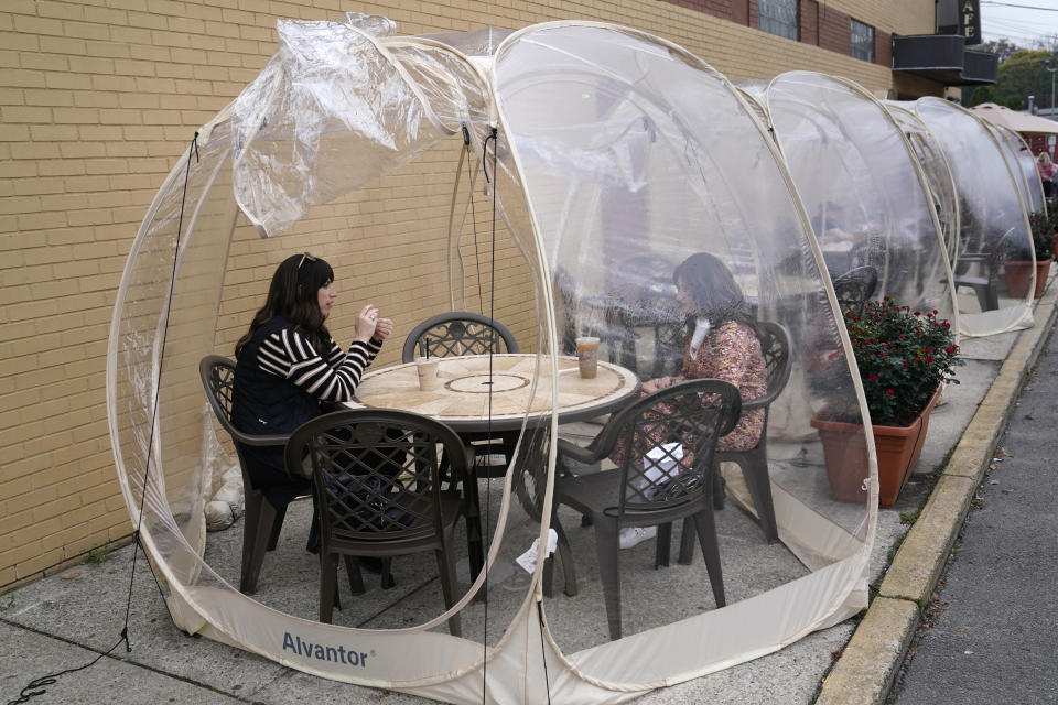 Aviva Markowitz, left, and Rivka Alter enjoy a drink in a protective bubble at the Lazy Bean Cafe in Teaneck, N.J., Thursday, Oct. 22, 2020. The bubbles have been popular with customers, both for social distancing and warmth as the weather turns colder. New Jersey's climbing number of COVID-19 cases are beginning to spread to northern counties around New York, Gov. Phil Murphy said Thursday. Essex, Union, Hudson and Bergen counties reported more than 100 new cases overnight, Murphy said, eclipsing recent hot spots in Ocean and Monmouth counties. (AP Photo/Seth Wenig)