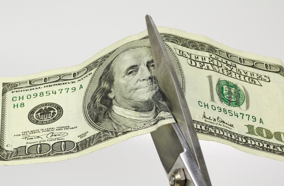 Scissors cutting through a hundred dollar bill.