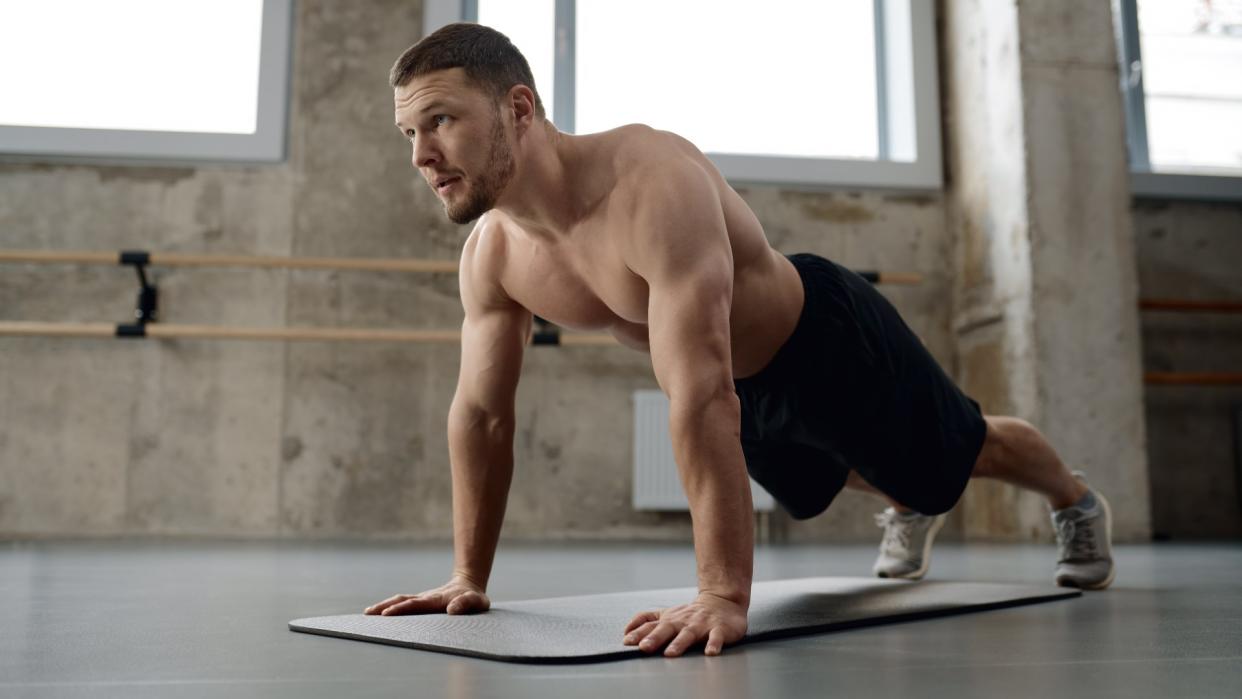  Young athletic man doing push-ups physical workout in gym. 